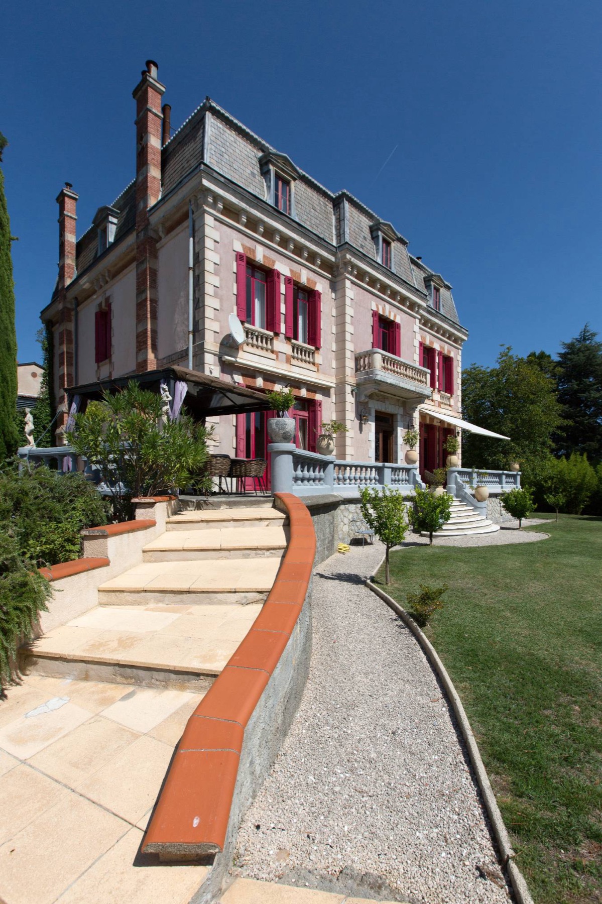 The château façade with raspberry shutters, stone balustrades and a curved staircase leading down to the lawn