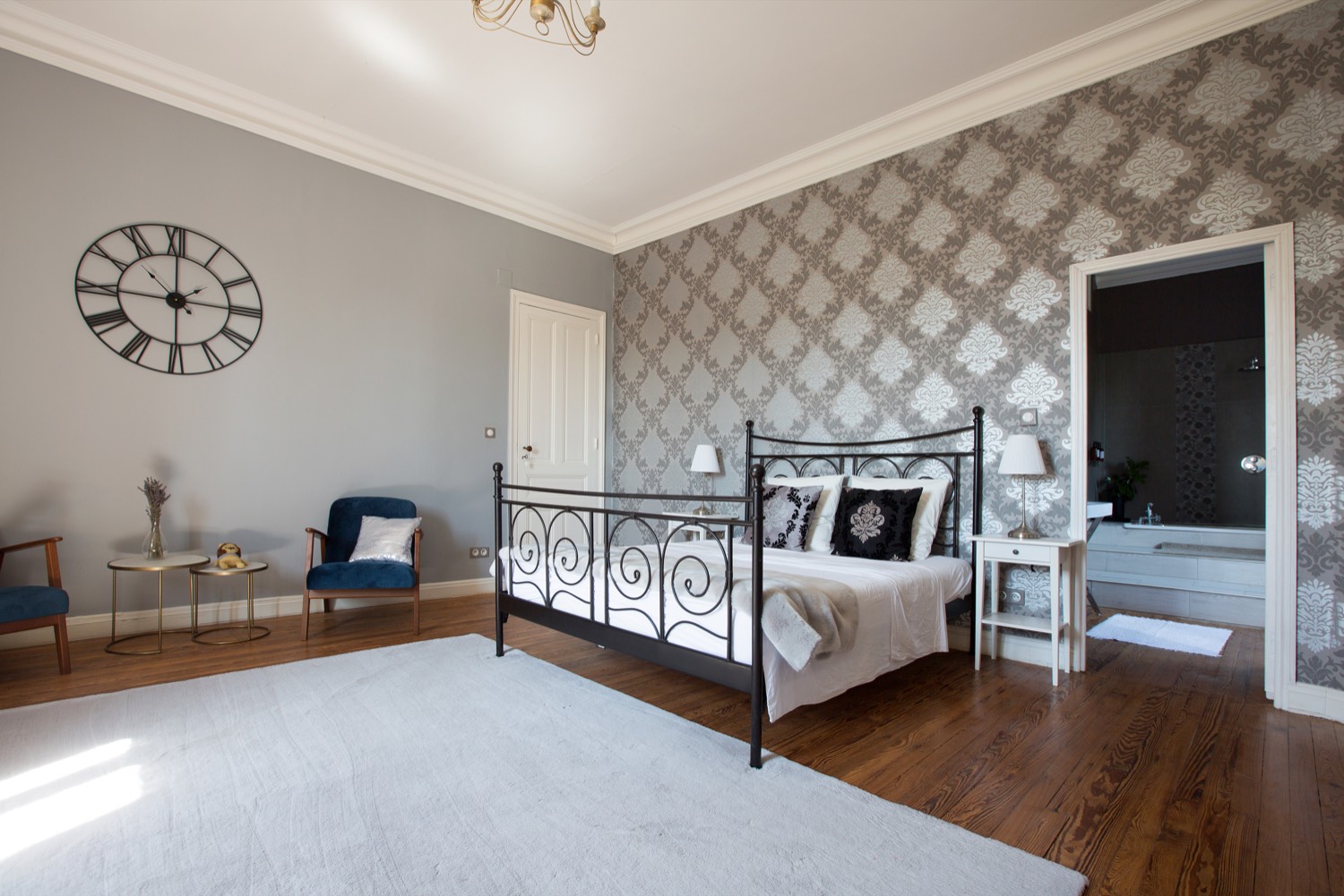 Bedroom with a black iron bed, grey damask wallpaper and a large wall clock