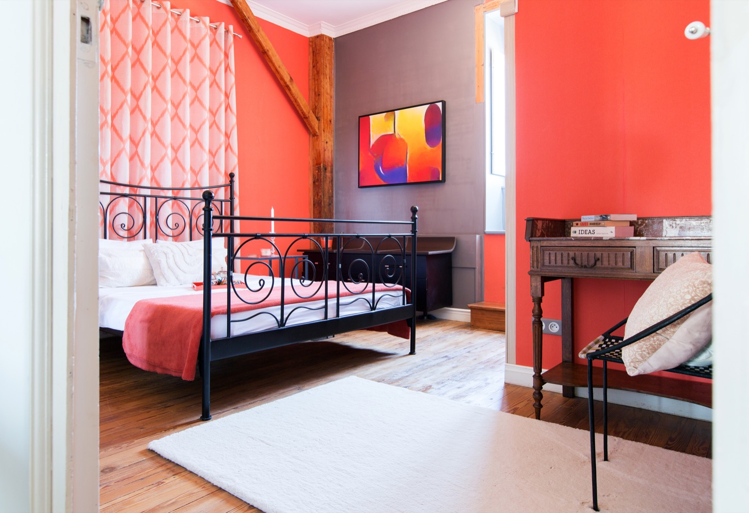 Bedroom with coral walls, an iron bed and a colourful painting