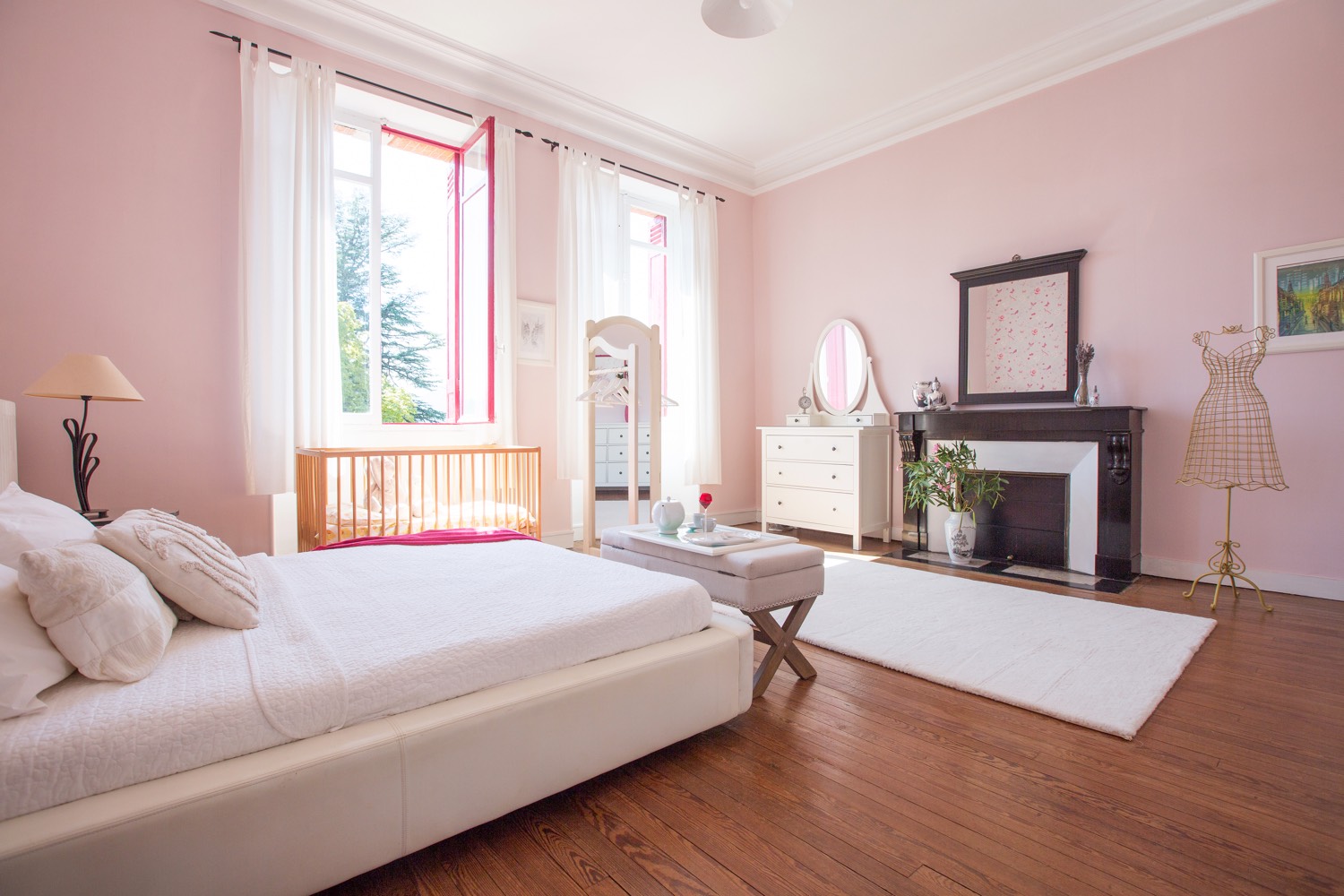 Pale pink bedroom with a large bed, a fireplace and tall windows onto the garden