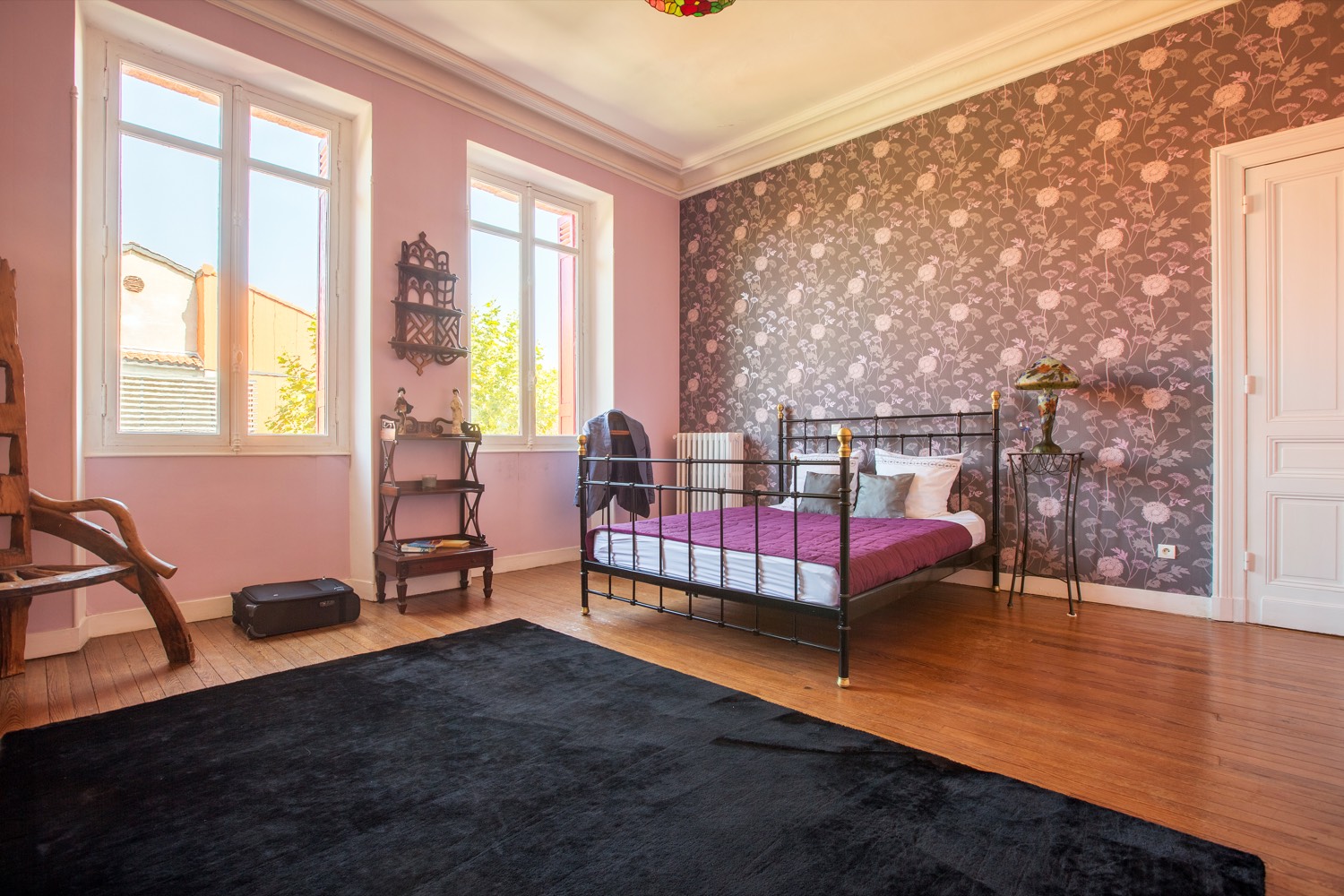 Bedroom with floral wallpaper, an iron bed and two tall windows