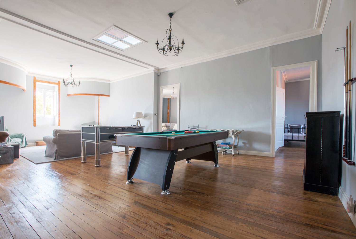 Games room with a pool table, wooden floors, chandeliers and sofas
