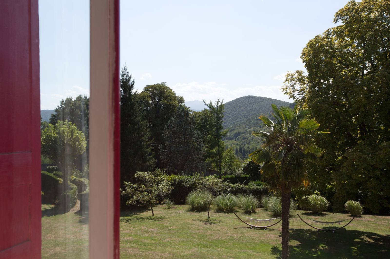 View from a window across the lawn with hammocks and a palm tree to wooded hills