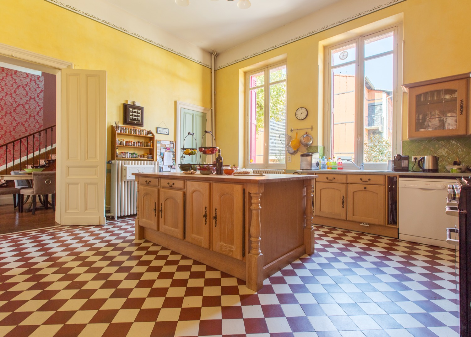 Kitchen with a red and cream chequered floor, wooden island and tall windows