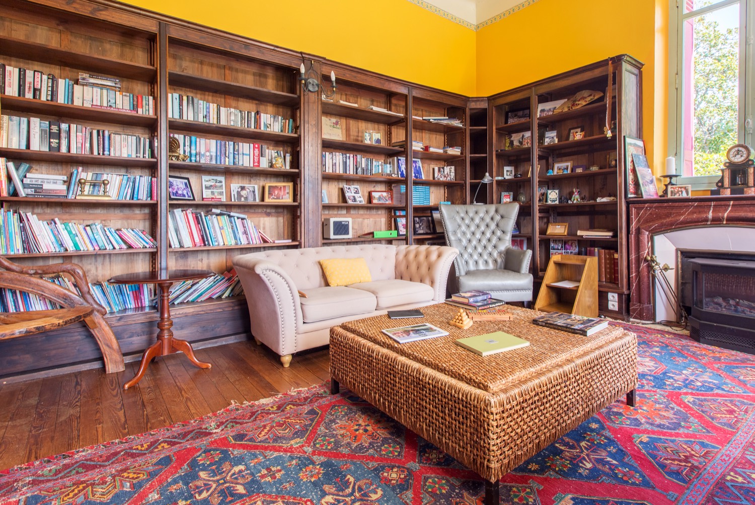 Library with wooden bookshelves, a sofa, an armchair and a fireplace