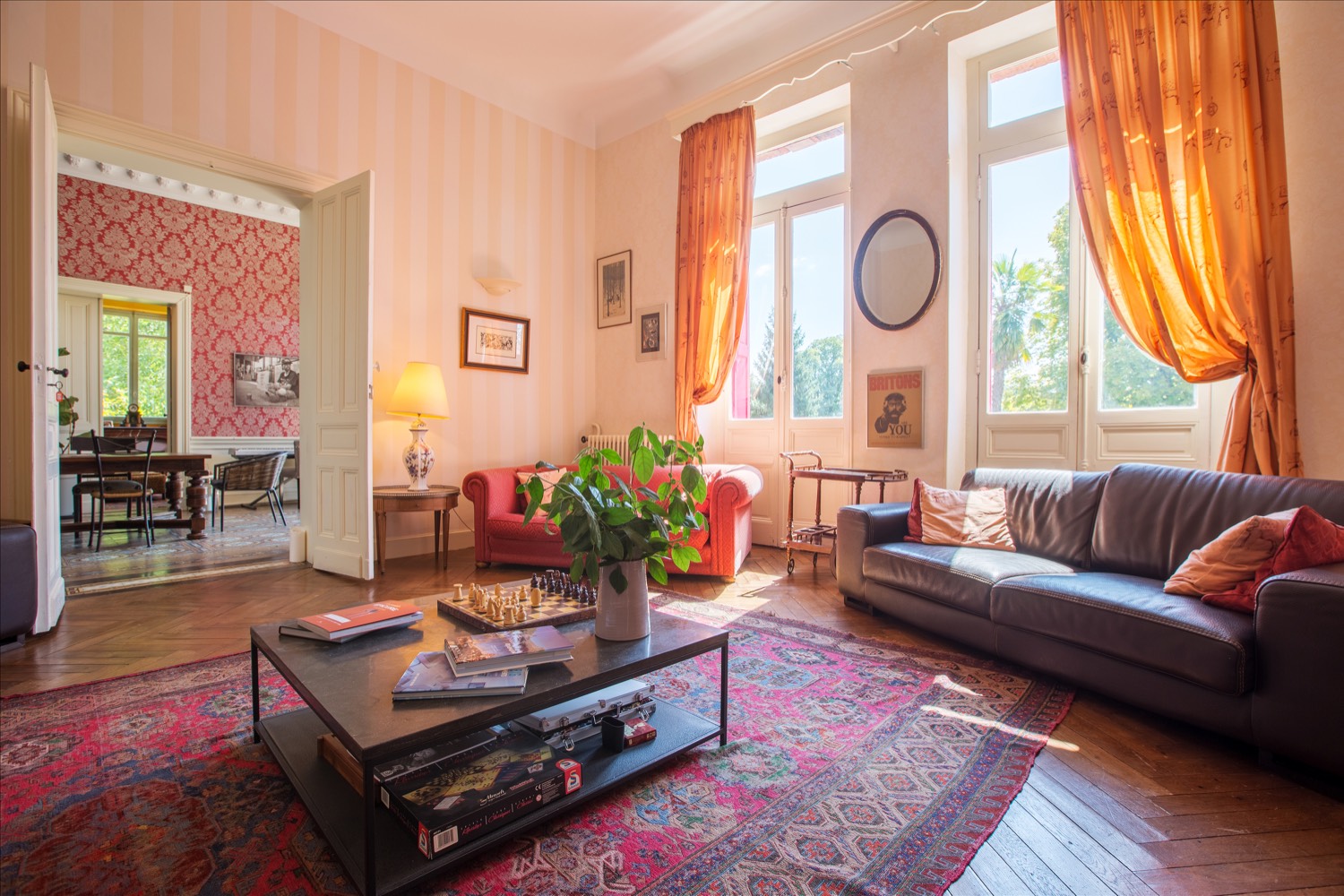 The grand salon with sofas, a chess table, Persian rug and tall windows