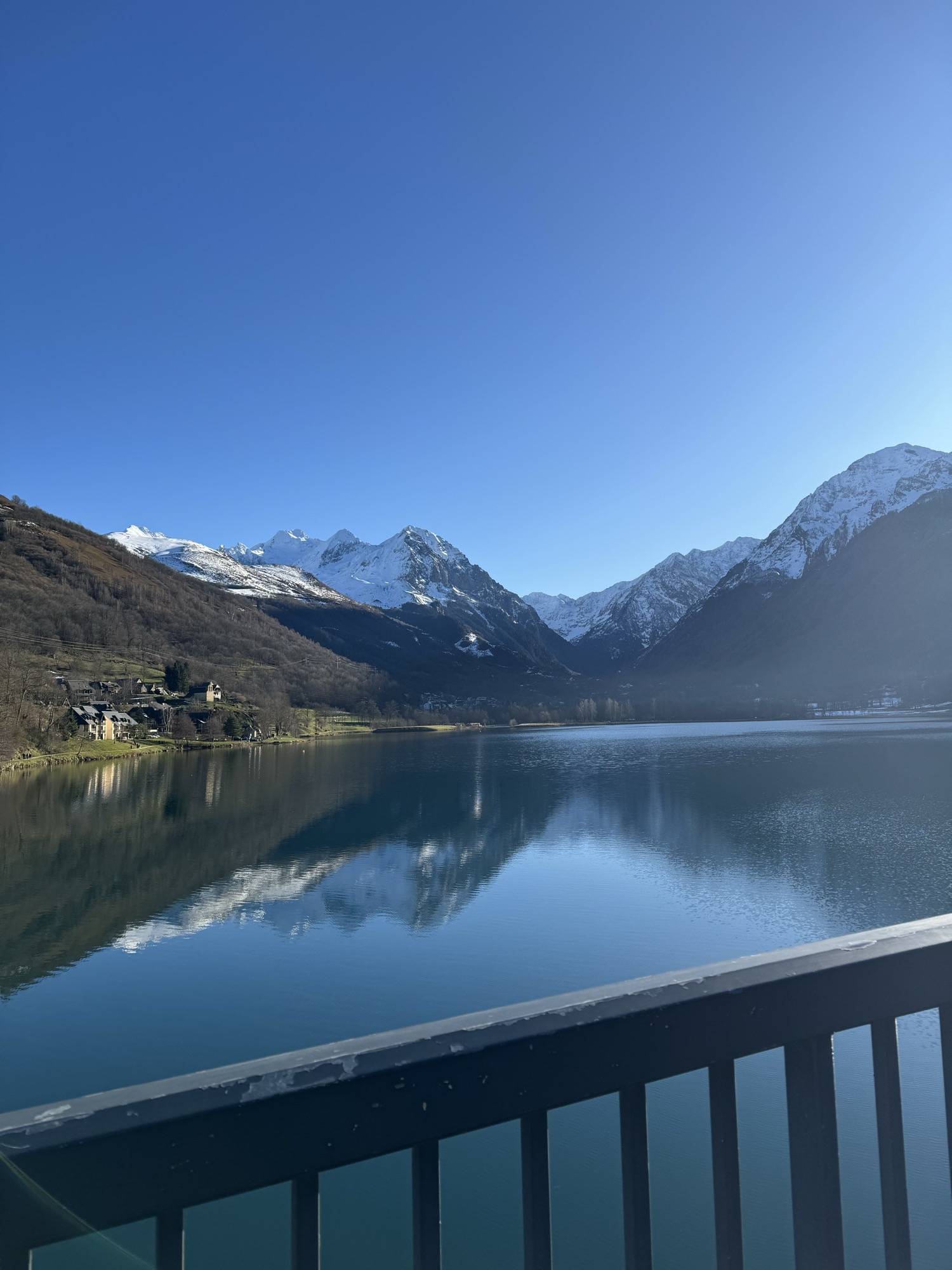 A still mountain lake reflecting snow-capped Pyrenean peaks under a clear blue sky