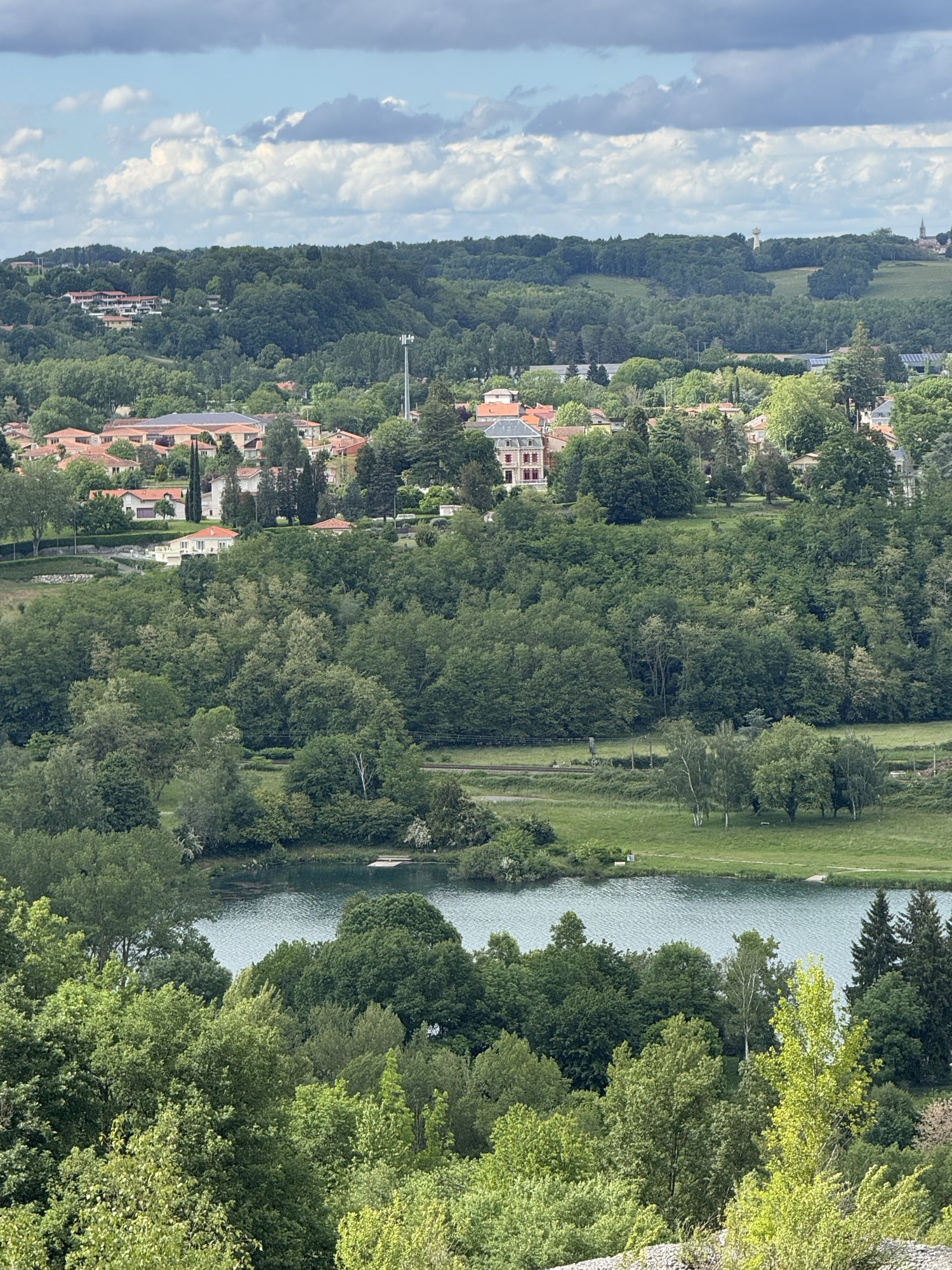 A wooded green valley with a lake, with Le Château Rouge among the houses on the hillside